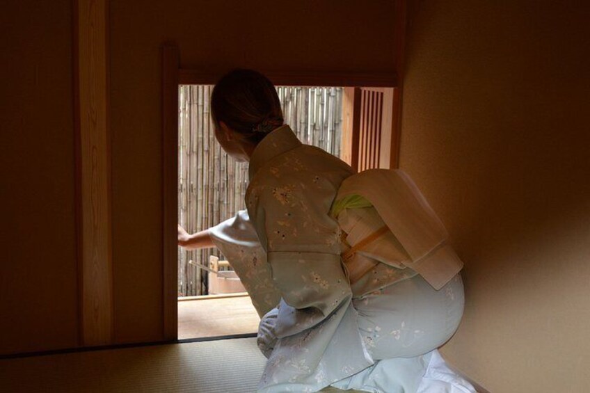 A person in traditional attire, possibly performing a cultural activity, in a room with wooden walls and a sliding door. 4