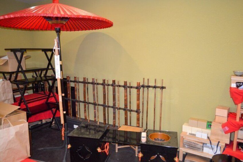 A room with a red umbrella, bamboo sticks, a black table, and boxes. 5