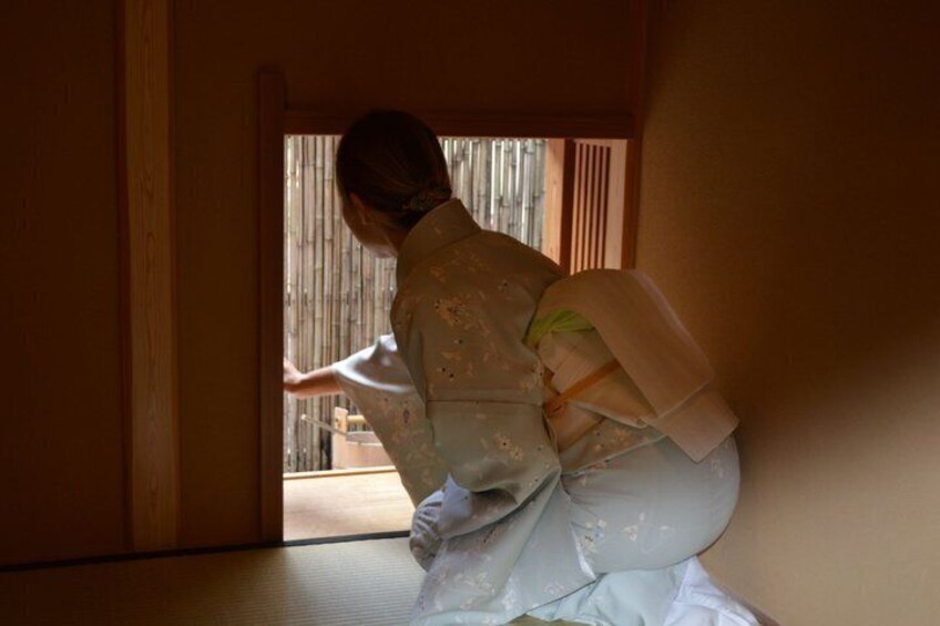 A person in traditional attire, possibly performing a ritual or ceremony, in a room with wooden walls and a sliding door. 4