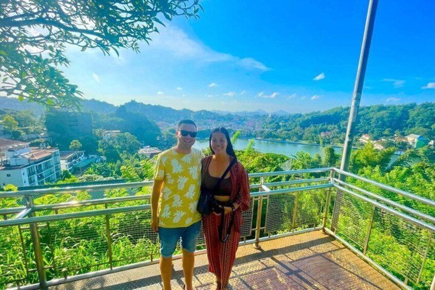 A couple standing on a balcony overlooking a river and greenery. 2