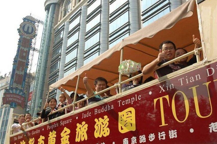 A double-decker bus with passengers, a sign for Jade Buddha Temple, and a clock tower in the background. 4