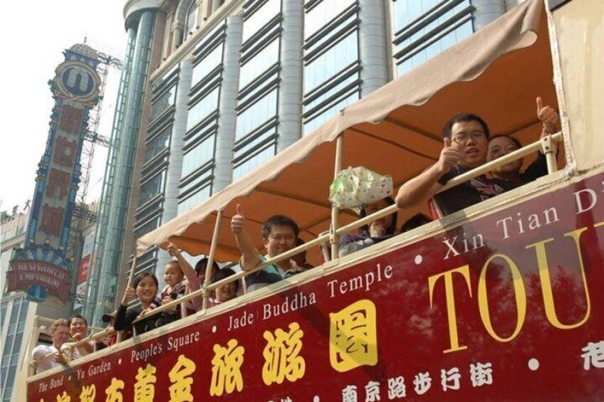 A double-decker bus with passengers, a sign for the Jade Buddha Temple, and a clock tower in the background. 4