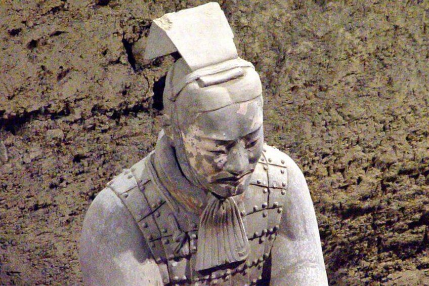 Una estatua de terracota de un guerrero con armadura, frente a un fondo rocoso. 4