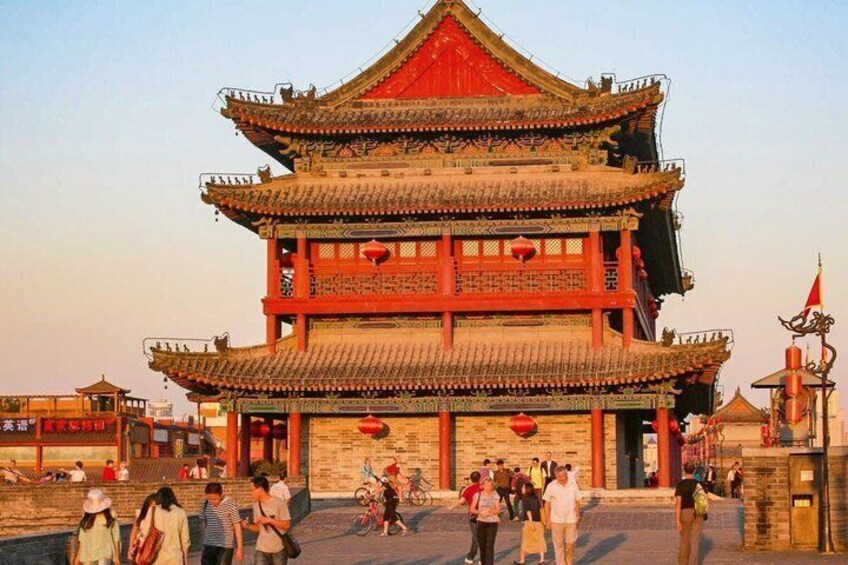 A traditional multi-tiered building with red and grey roofing, surrounded by a paved area with people walking and sitting. 2