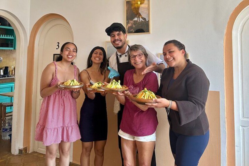 A group of people holding plates with food in a room with arched doorways and a number on the wall. 2