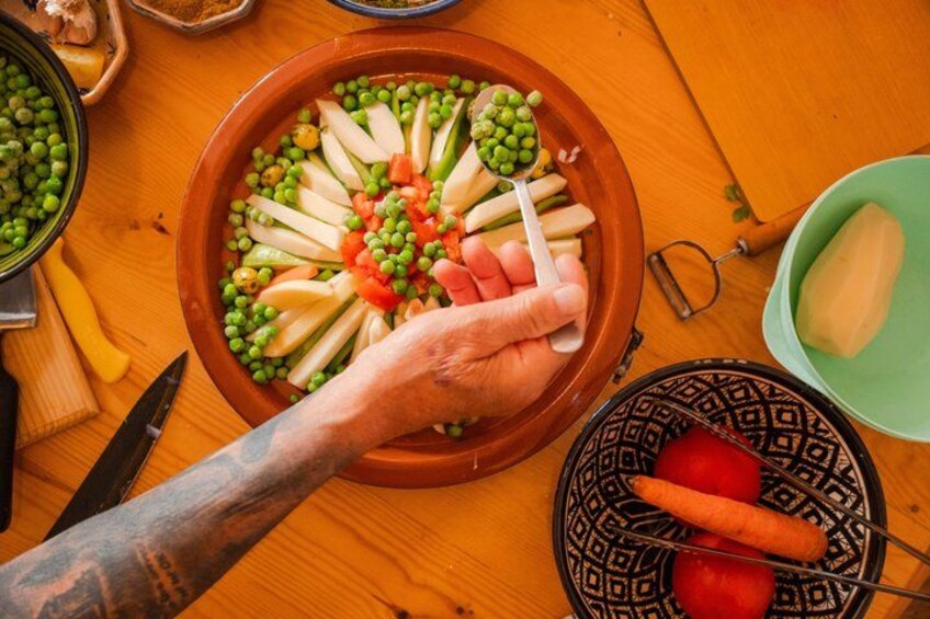 A wooden table with a ceramic dish containing sliced vegetables and a hand holding a spoon. 5
