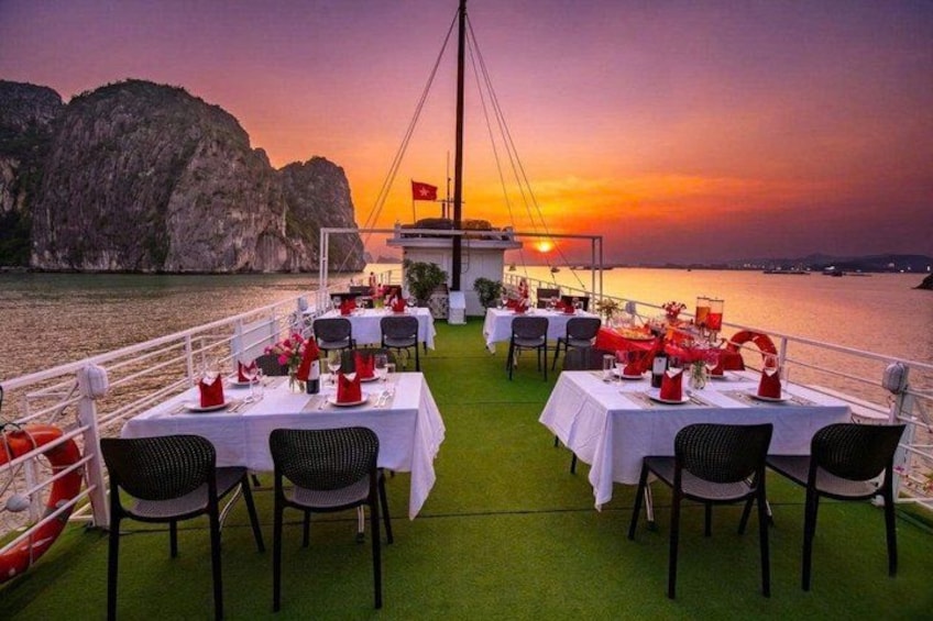 A sunset dining area on a boat with tables set for two, overlooking a body of water and a rocky coastline. 4
