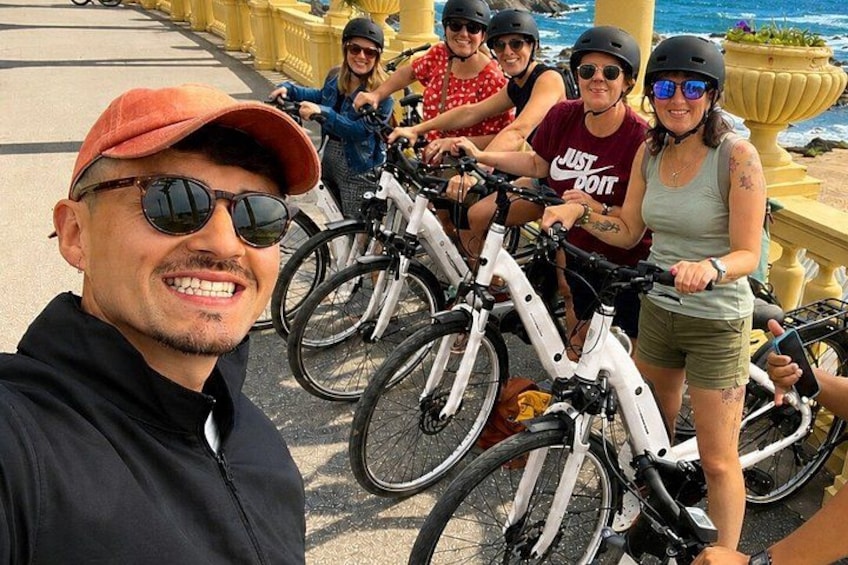 A group of people on bicycles, a coastal promenade, and a body of water in the background. 4