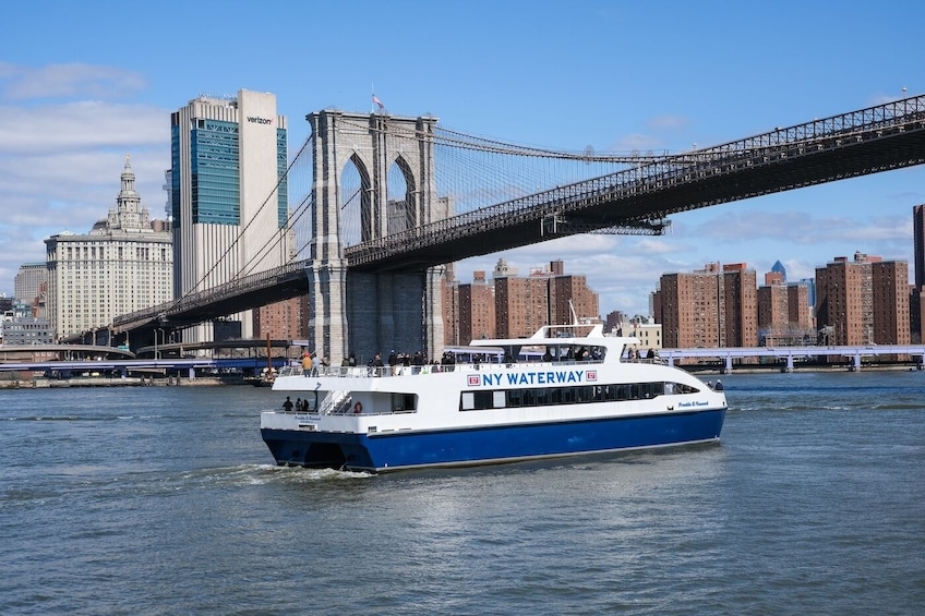 A ferry named NY Waterway passing under the Brooklyn Bridge with a city skyline in the background. 1