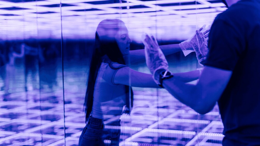A person in a dark shirt and jeans, reaching out to another individual in a purple-lit environment. 3