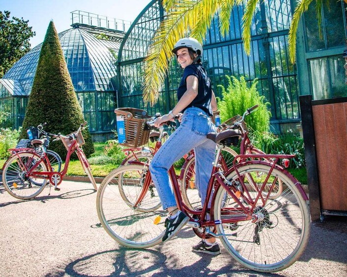 A person riding a red bicycle in a greenhouse with glass walls and a conical tree. 3