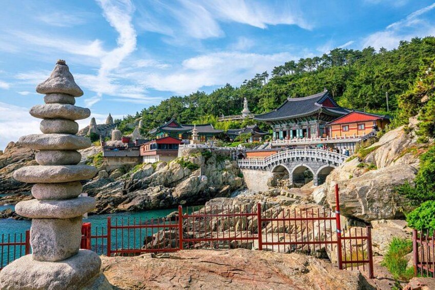 A traditional Korean temple with a stone stack, a bridge, and a red fence. 4