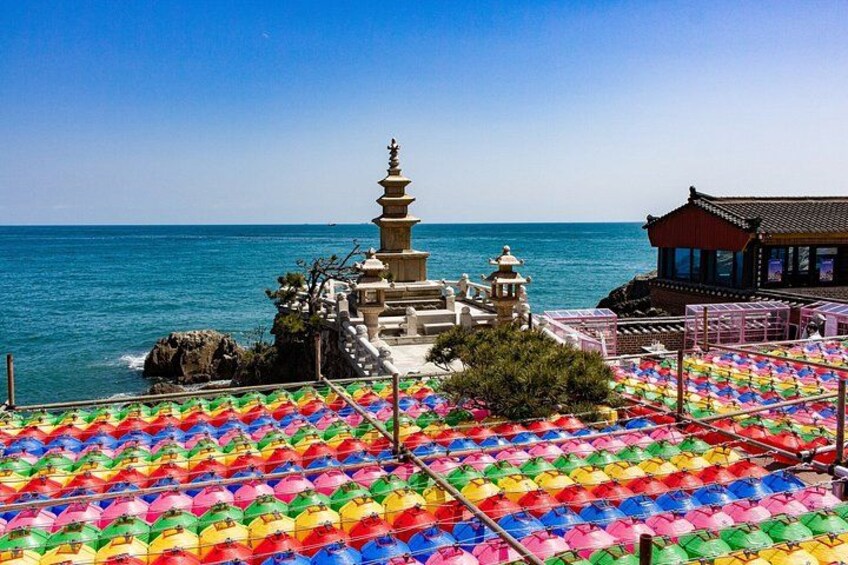 A coastal temple with a pagoda, colorful umbrellas, and a clear blue sky. 3