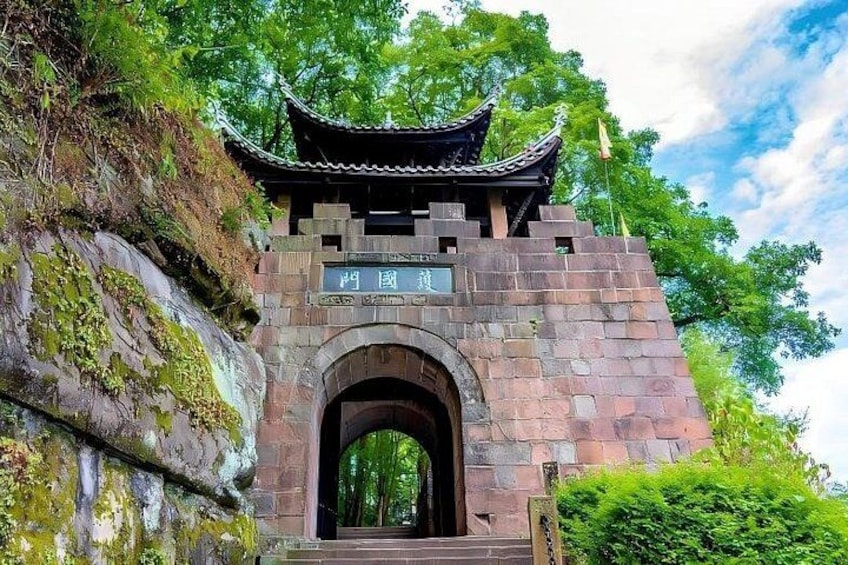 A traditional Chinese gate with a curved roof, set against a backdrop of lush greenery and a clear sky. 5