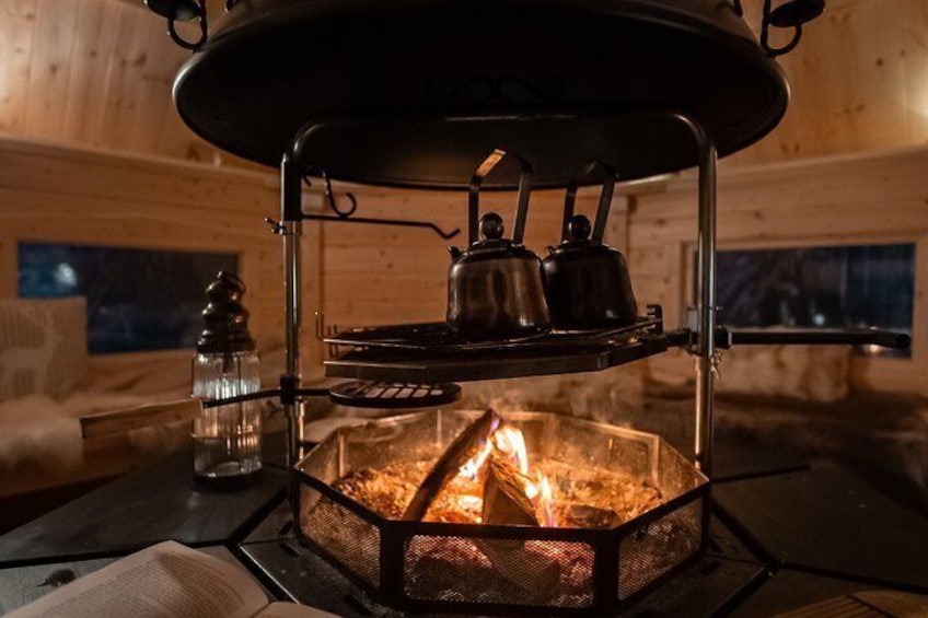 A wood-burning stove with kettles and a glass container on a metal rack. 2
