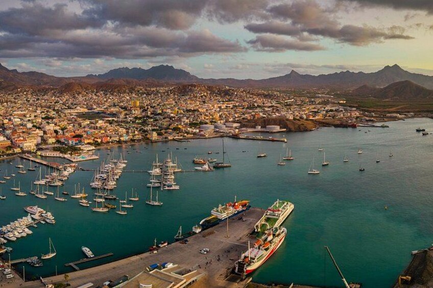 A coastal town with a marina filled with boats, a large ship docked at the harbor, and mountains in the background. 5
