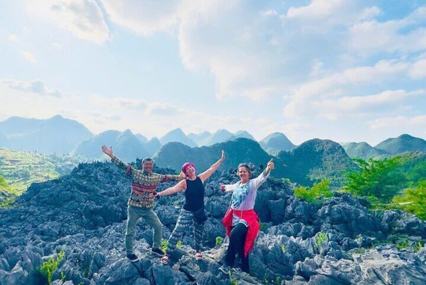 Three people standing on rocky terrain with mountains in the background. 1
