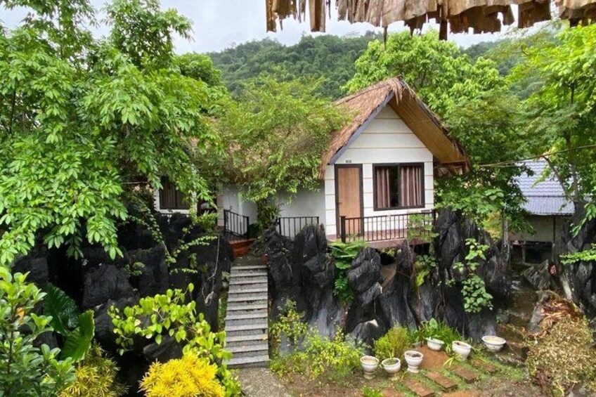 A thatched-roof house surrounded by lush greenery and rocky terrain. 3