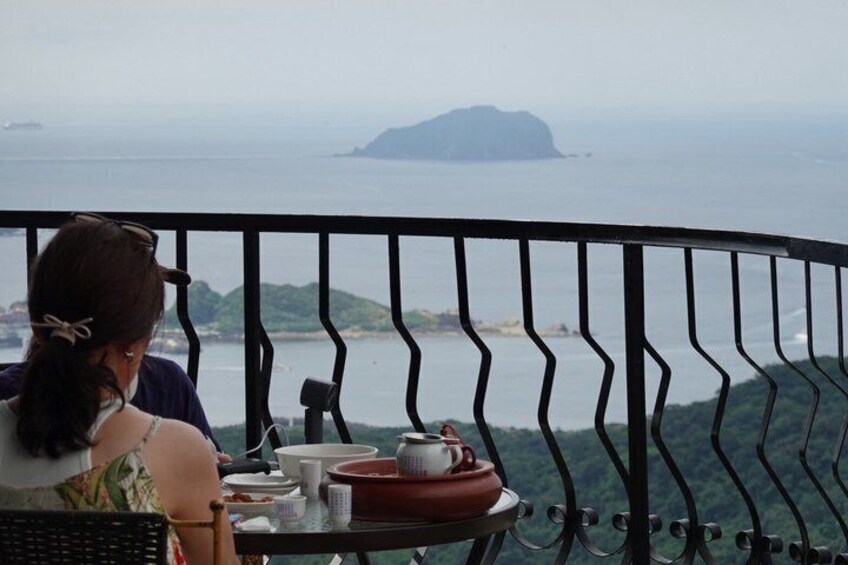A person sitting at a table with a view of the sea and a distant island. 1
