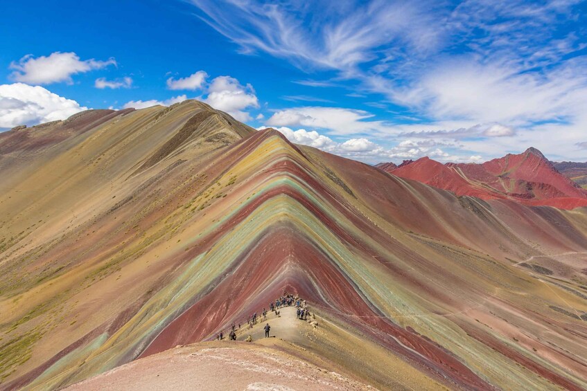 A mountain range with colorful stratified layers and a group of people at the base. 2