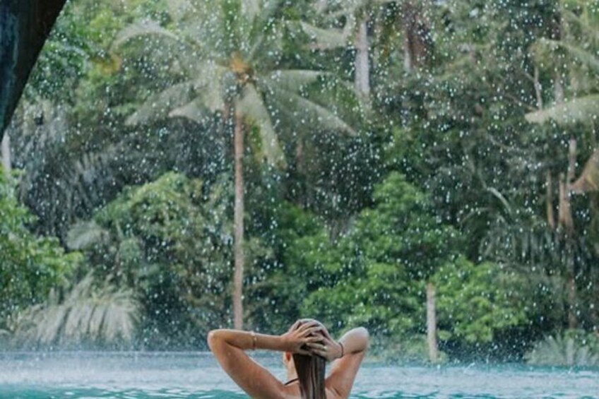 A person relaxing by a pool with palm trees and a waterfall in the background. 5