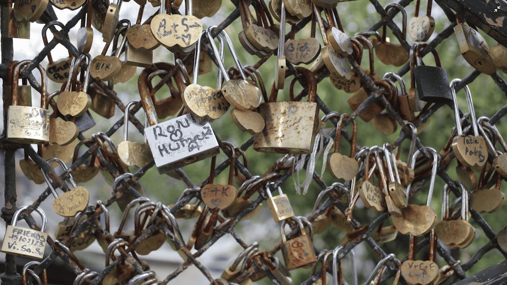 A chain of padlocks, some with names and dates, attached to a fence. 4