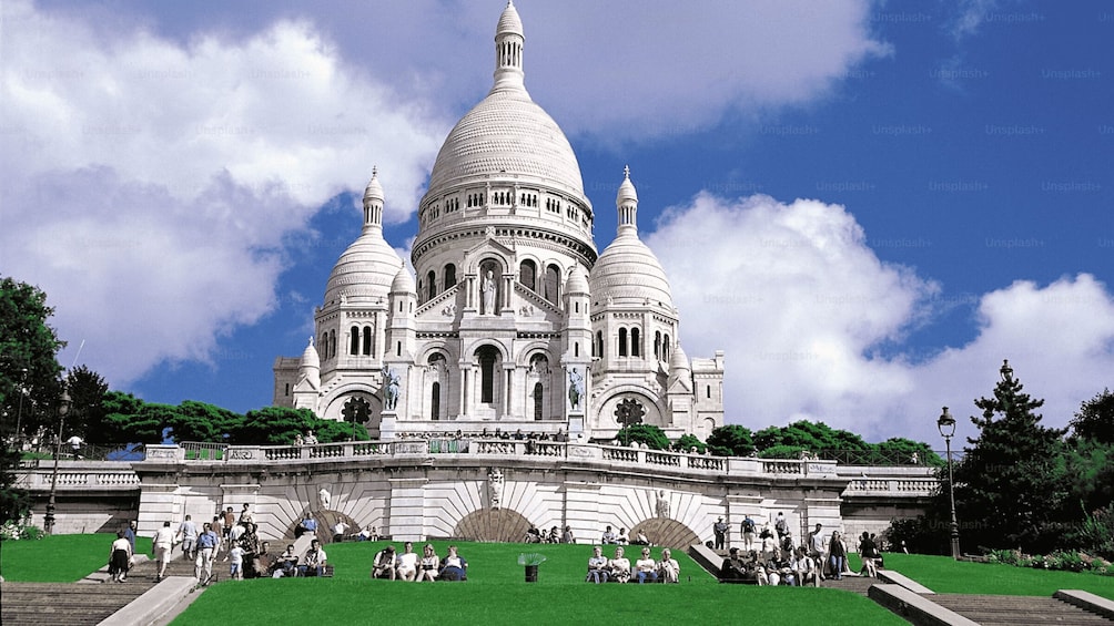A large white domed building with a central dome and two smaller domes, surrounded by a green lawn and a stone bridge. 1