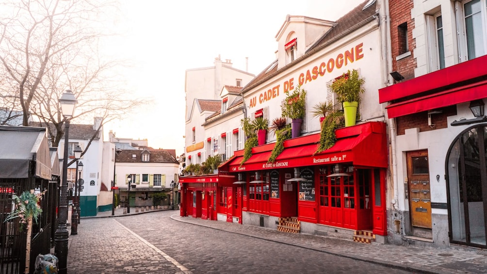 A cobblestone street with red awnings and a building with 'Au Cadet de Gascogne' signage. 3