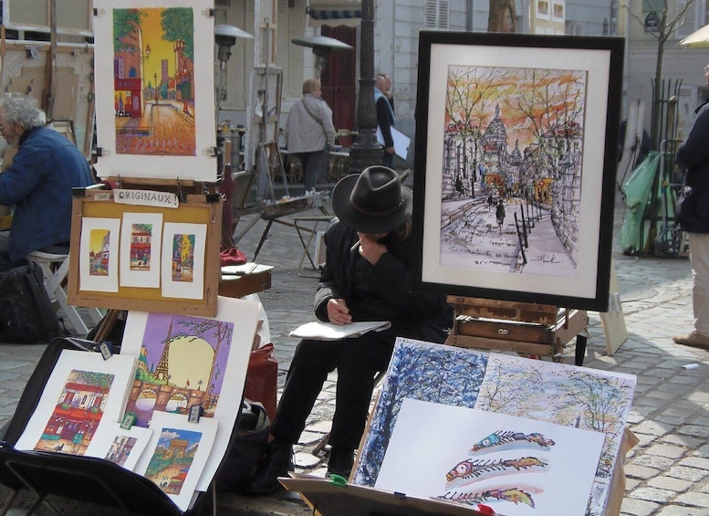 An artist painting outdoors with various artworks displayed around. 5