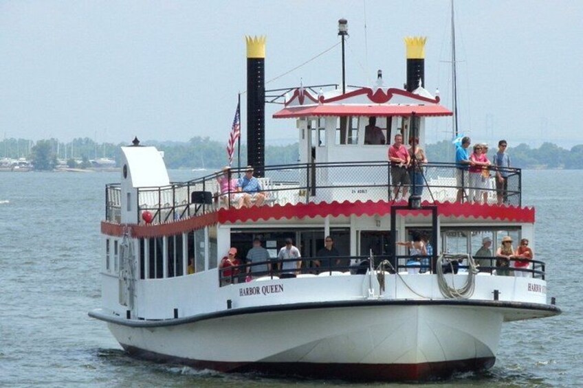 A white boat with red trim and the name 'Harbor Queen' on the side, sailing on water with a city skyline in the background. 5
