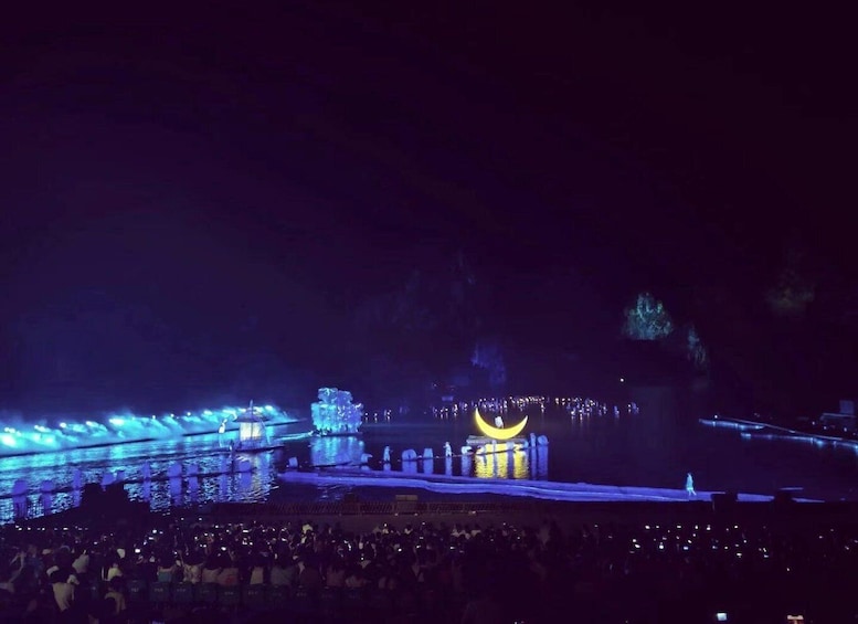 A nighttime outdoor event with a stage, audience, and illuminated structures. 3