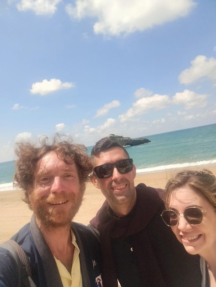 Three people on a beach with the ocean and a rocky outcrop in the background. 4