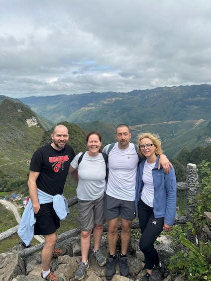 Four people standing on a rocky outcrop with a mountainous landscape in the background. 2