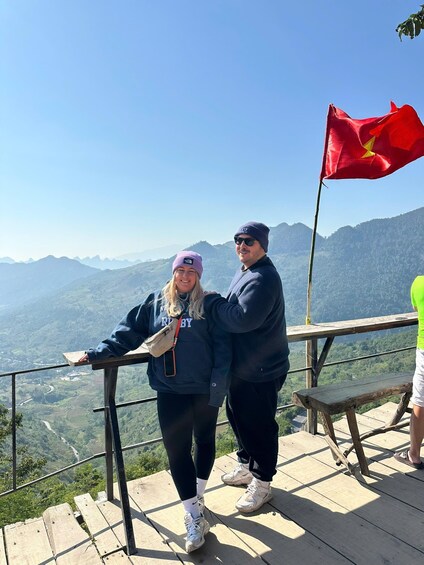 Two people standing on a wooden platform overlooking a mountainous landscape. 3