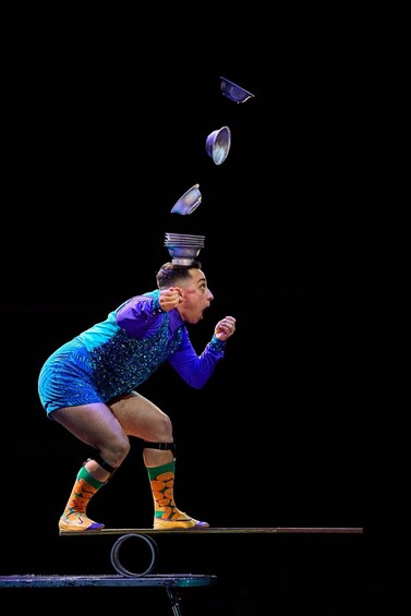 A person in a blue and purple outfit with colorful socks, balancing on a drumstick. 4