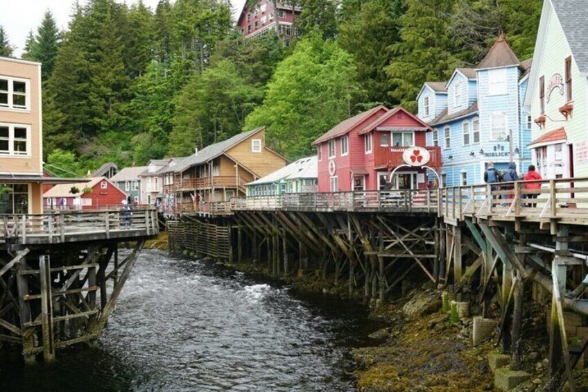 A wooden bridge over a river, colorful houses, and a forested hillside. 1