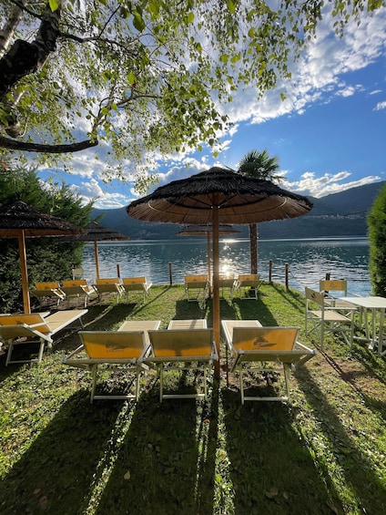 A lakeside terrace with lounge chairs and thatched umbrellas, overlooking a calm lake and distant mountains. 2