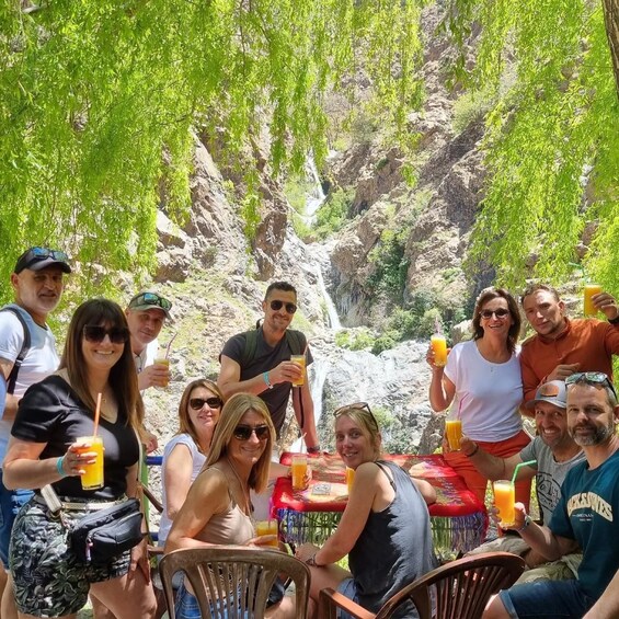 A group of people sitting around a table outdoors with a waterfall in the background. 1