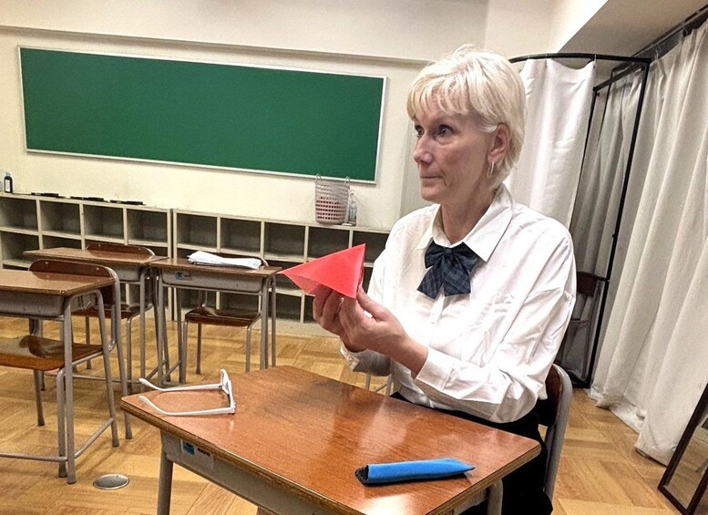 A classroom with desks, a chalkboard, and a person holding a red object. 5