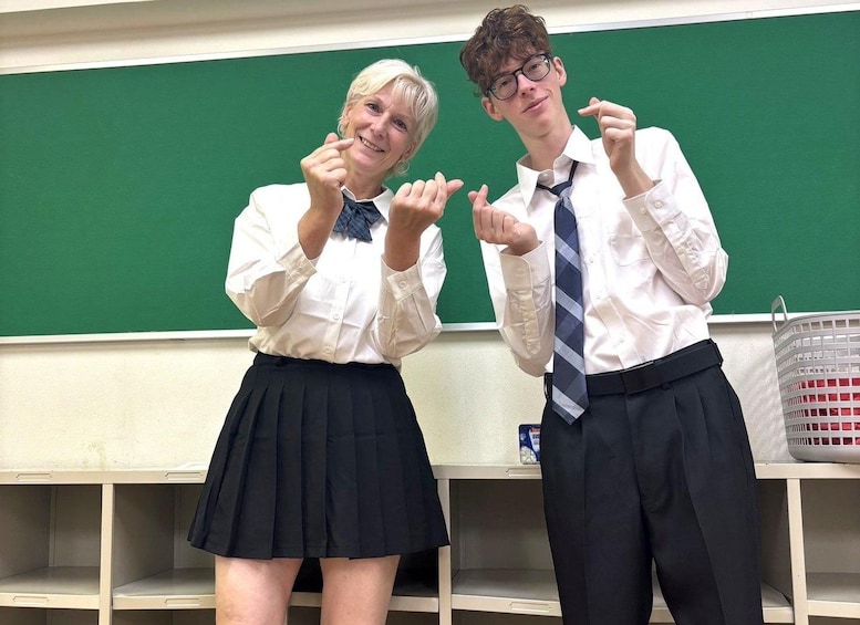 Two individuals in a classroom, one pointing at the other, with a green chalkboard and a whiteboard in the background. 1