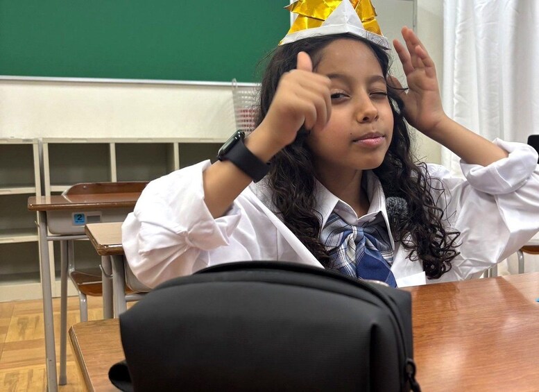 A classroom with a student wearing a school uniform and a paper crown. 2