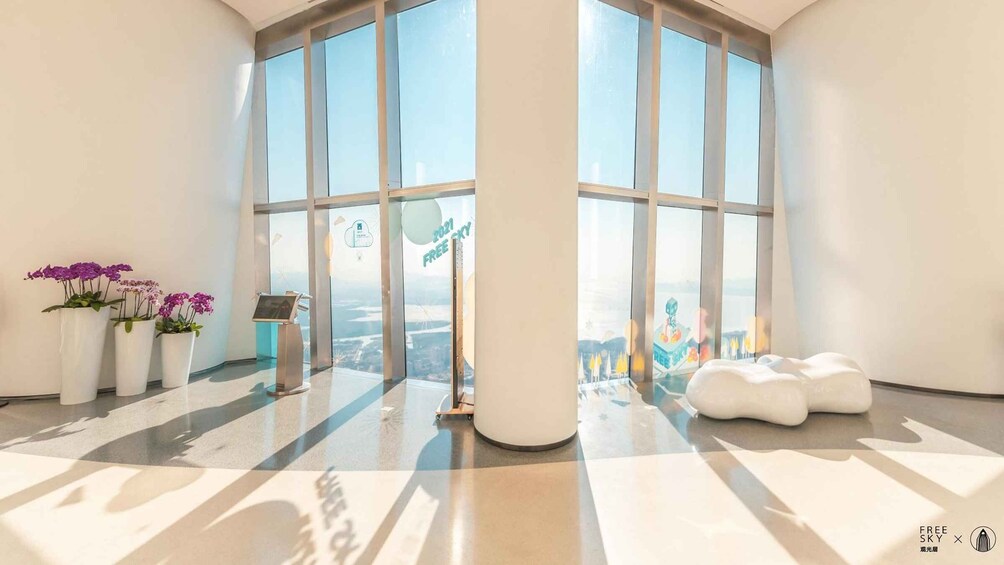A spacious room with large windows, a white floor, and several potted plants. 5