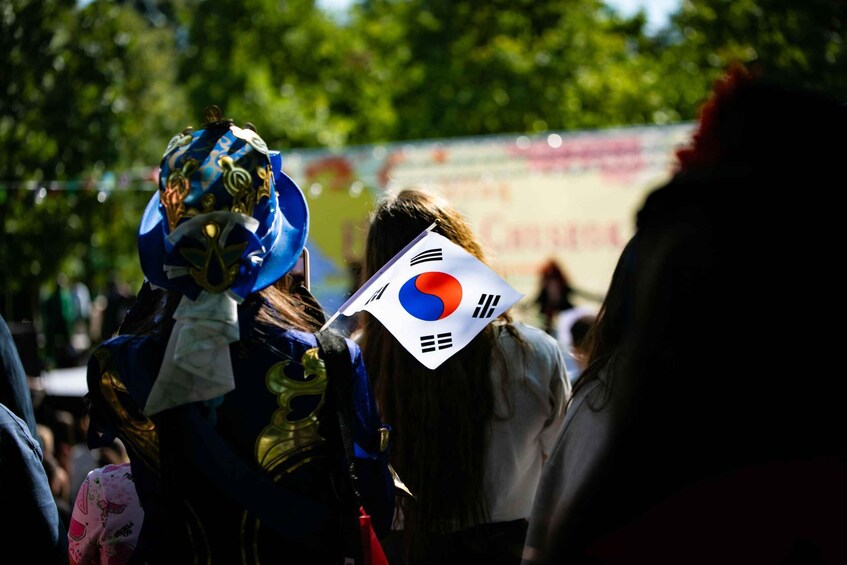 A crowd of people with some wearing blue and gold costumes and holding a flag with a red and blue circle and a white background. 2