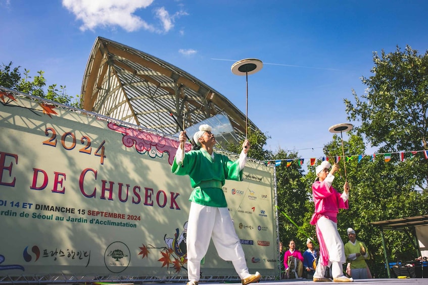 A cultural performance with performers in traditional attire on a stage with a backdrop displaying the event details. 4