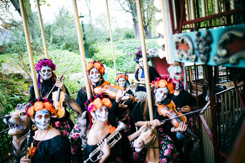 A group of people in a garden, some holding musical instruments, wearing colorful headpieces. 3