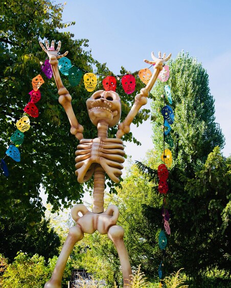 A skeleton sculpture with arms raised, surrounded by colorful skull decorations. 2