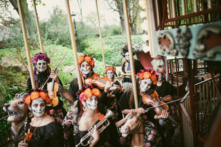 A group of people with painted faces and floral headpieces, playing string instruments. 1