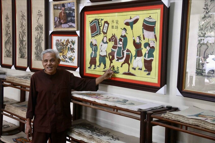 A person pointing at a colorful framed artwork with figures and text. 4