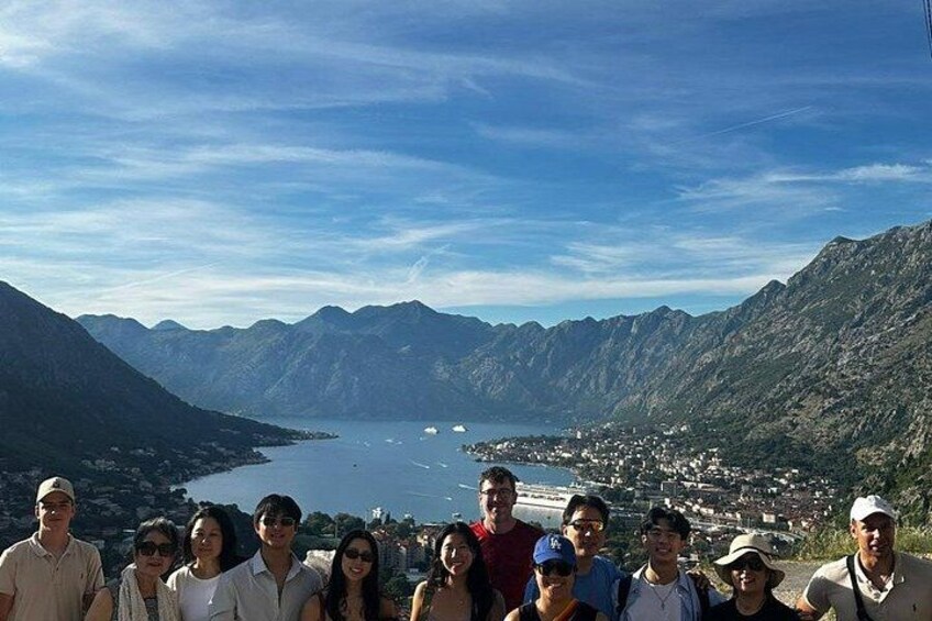 A group of people standing on a mountain overlooking a lake with a town in the distance. 3