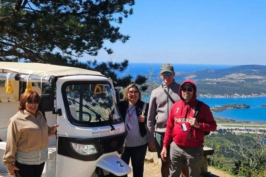 A group of people standing near a white vehicle with a canopy, overlooking a coastal landscape with hills and a body of water. 2